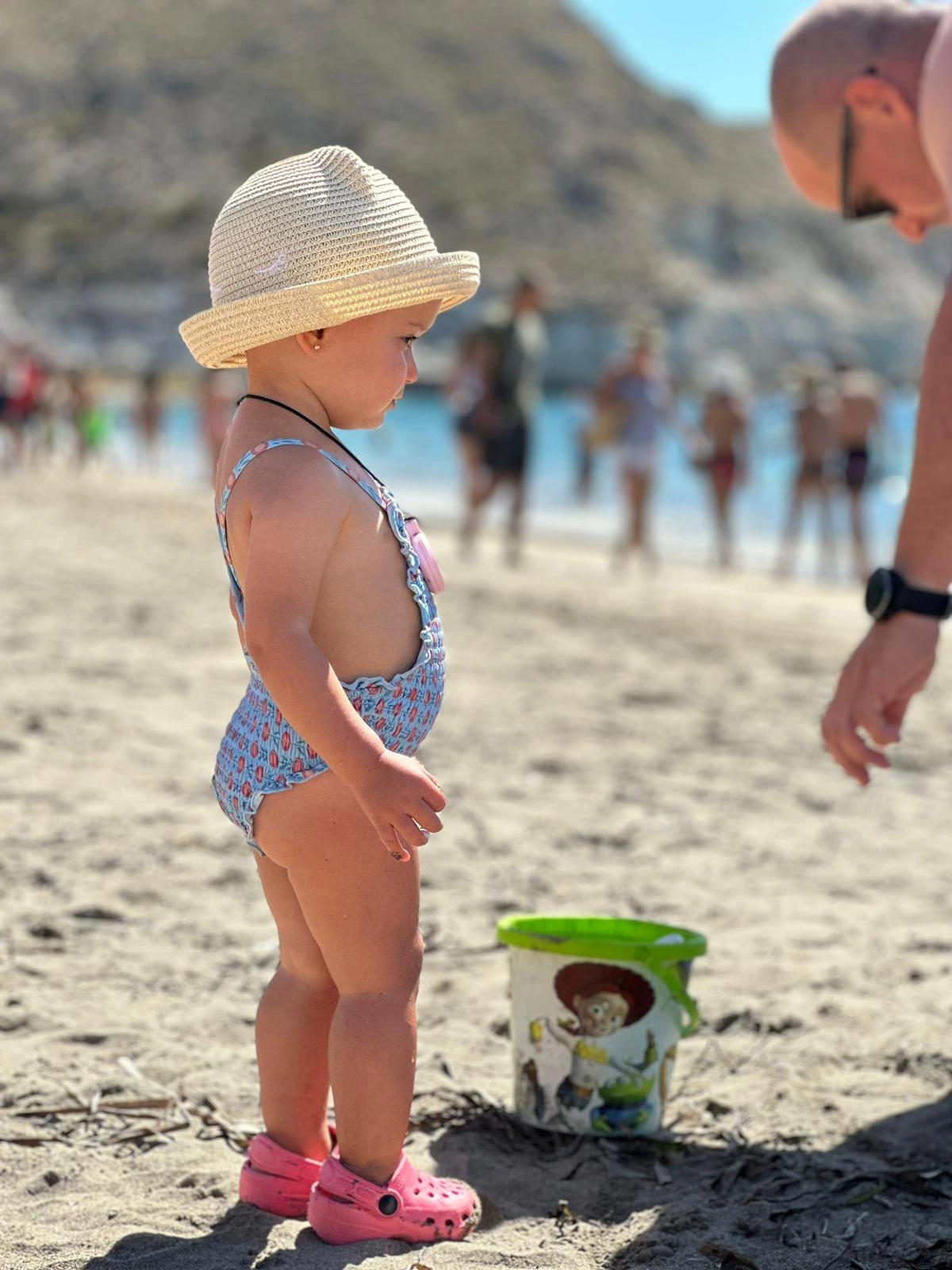 Original beach photograph of a child in a sun hat, with people and objects in the background