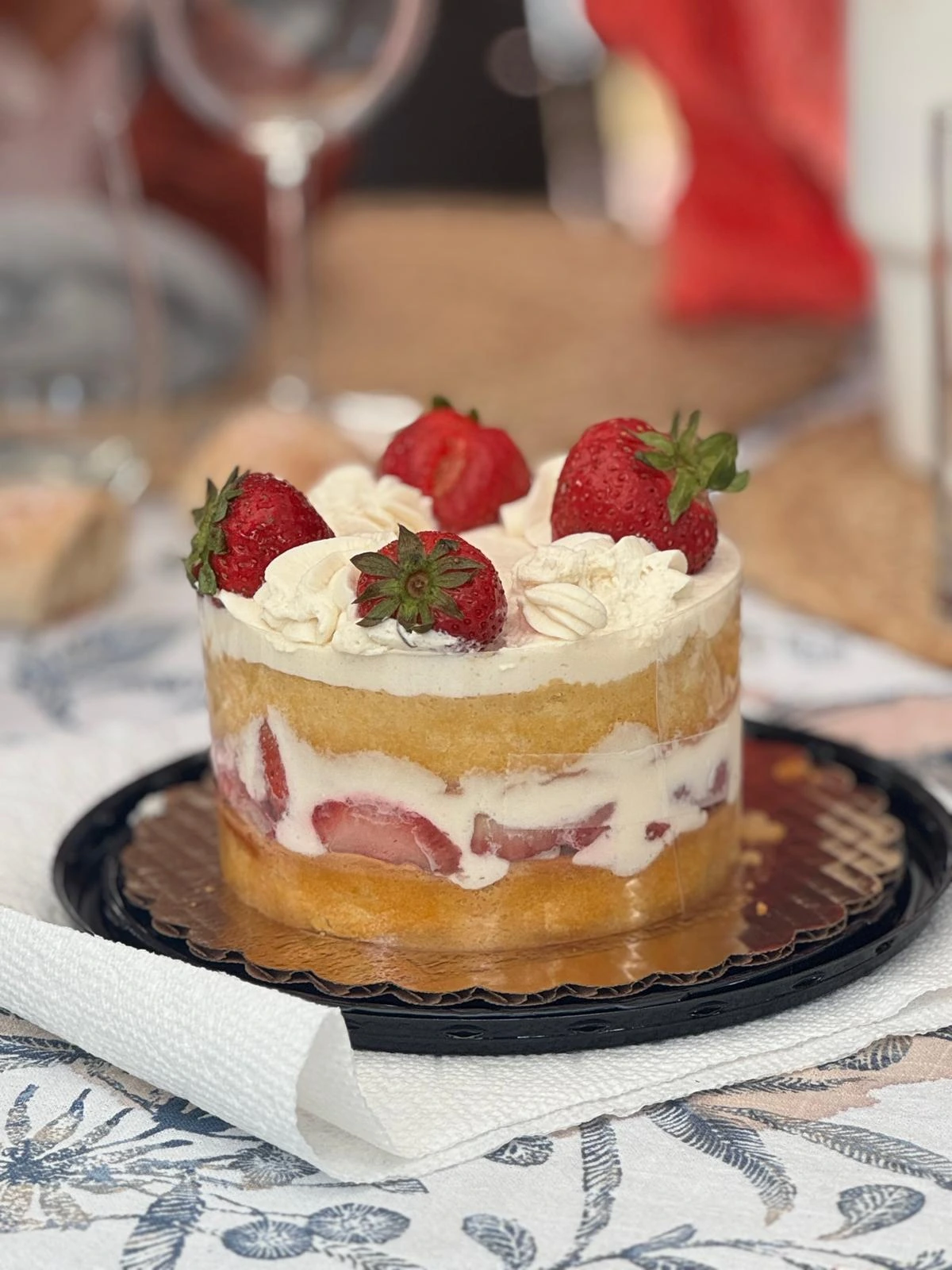 Original strawberry layer cake photographed on a table with a plastic tray and background distractions
