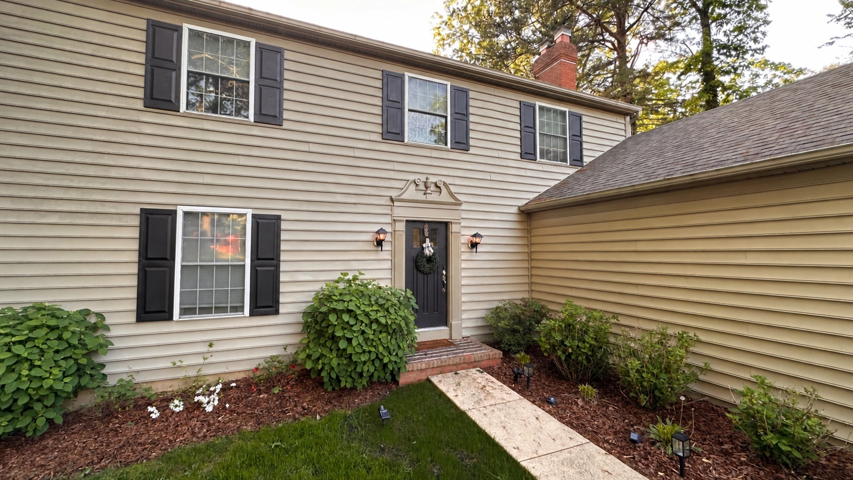 House exterior before retouching, with beige siding, dark shutters, existing shrubs, and the house number removed