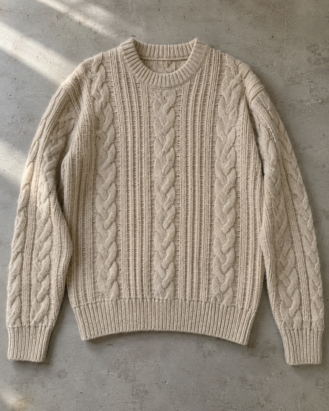 Generated casual product photograph of an oatmeal cable-knit sweater in uneven light